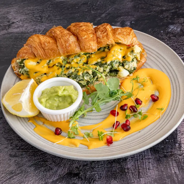 Breakfast croissant filled with spinach and egg, finished with hollandaise and avocado.