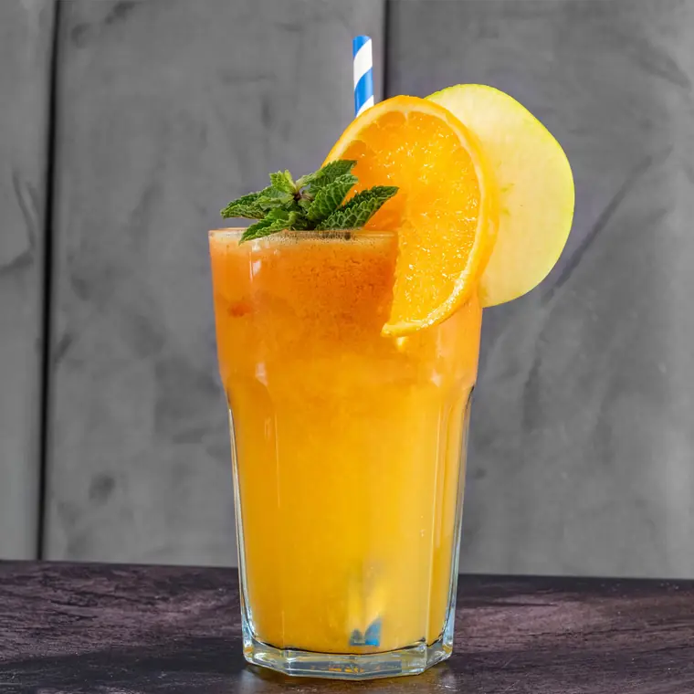 Fresh mixed juice in a tall glass with orange slices and mint.