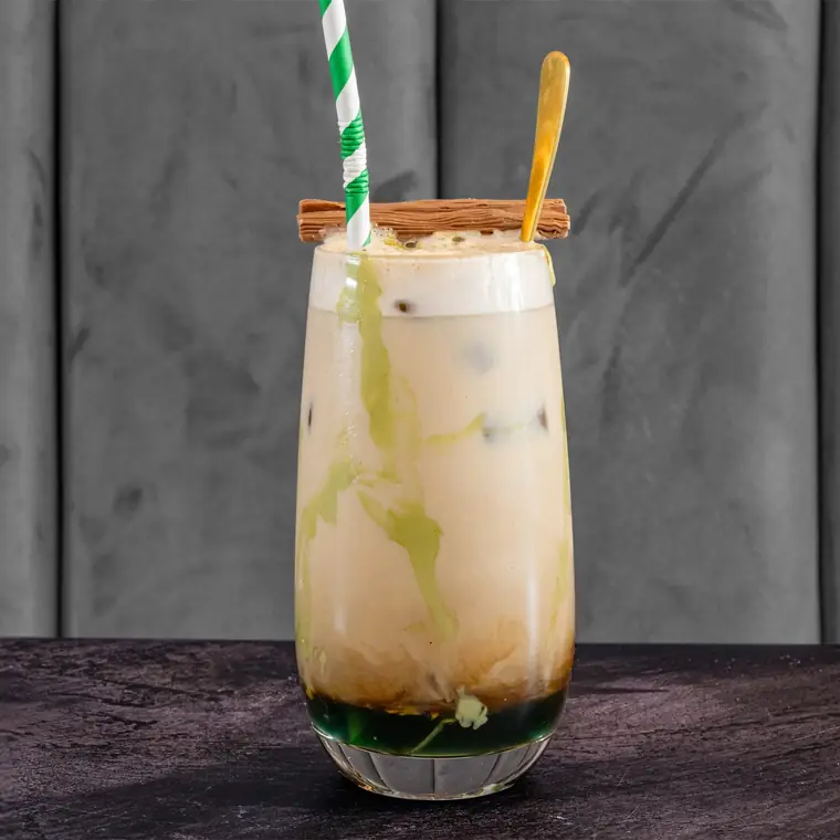Iced pistachio latte in a tall glass with a wooden spoon and mint.